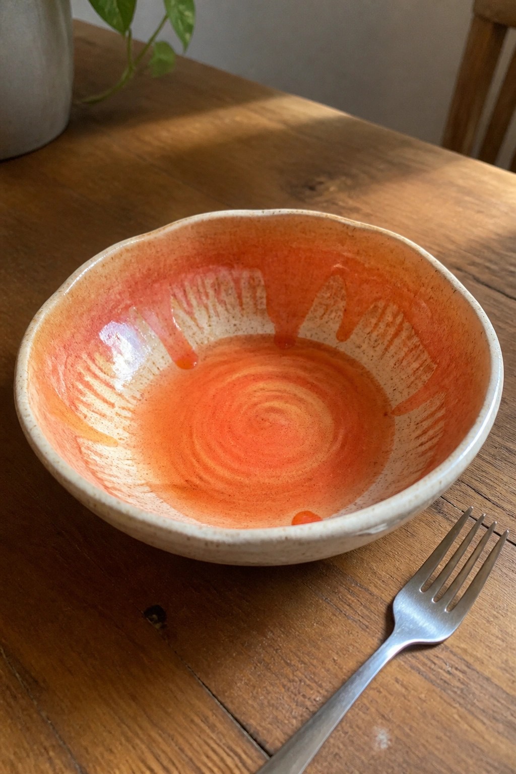 Orange ceramic bowl with sunburst glaze pattern beside fork on wooden table