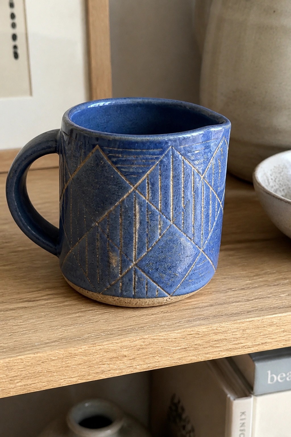 Blue ceramic mug with geometric etched patterns on wooden shelf