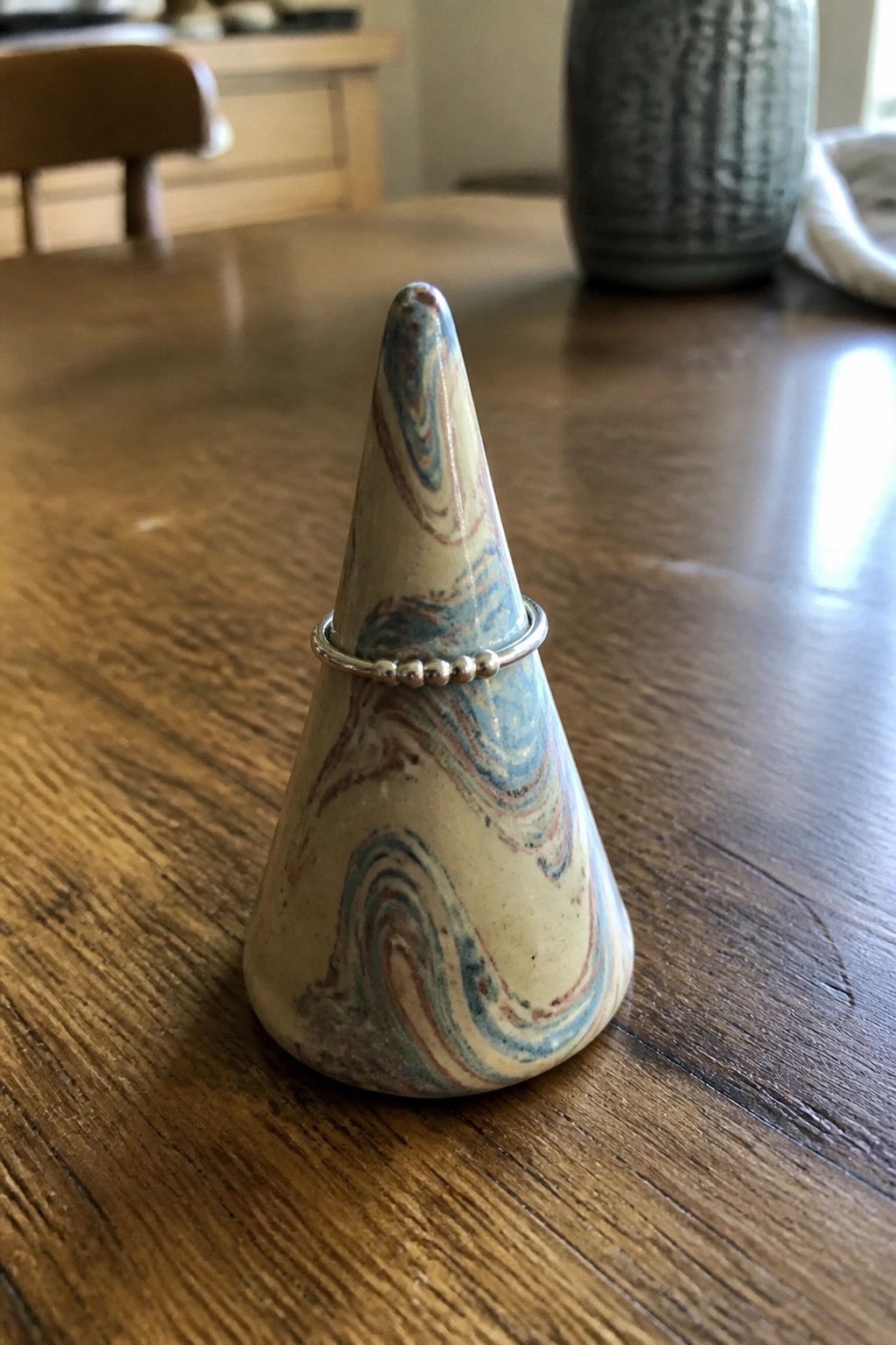 Marbled ceramic cone holding silver beaded ring on wooden table