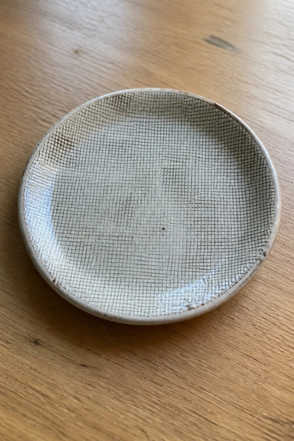 Small round ceramic dish with black grid pattern on wooden table