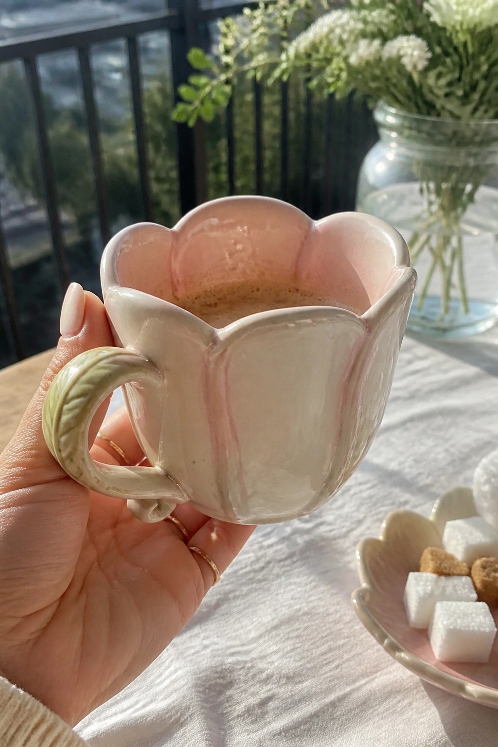 Hand holding pink floral ceramic mug with green handle beside sugar cubes.
