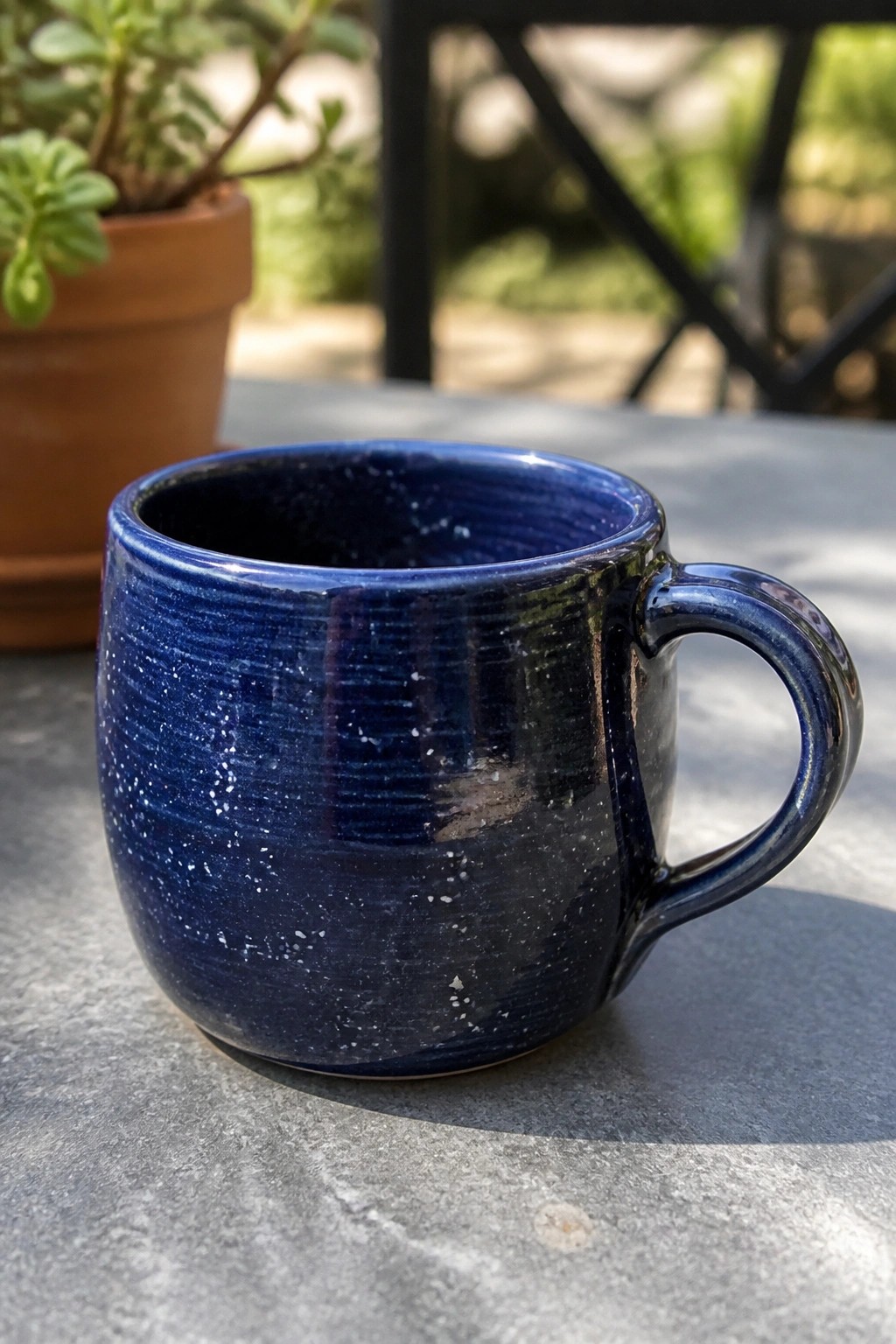 Blue speckled ceramic mug on gray table with potted plant behind.