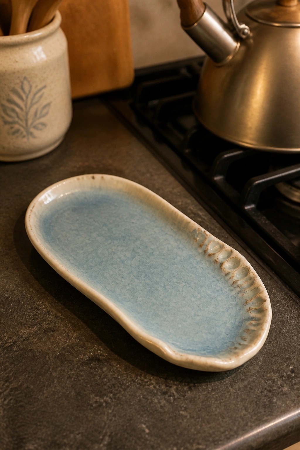 A light blue crackled ceramic oval dish rests on a dark countertop next to a stove.