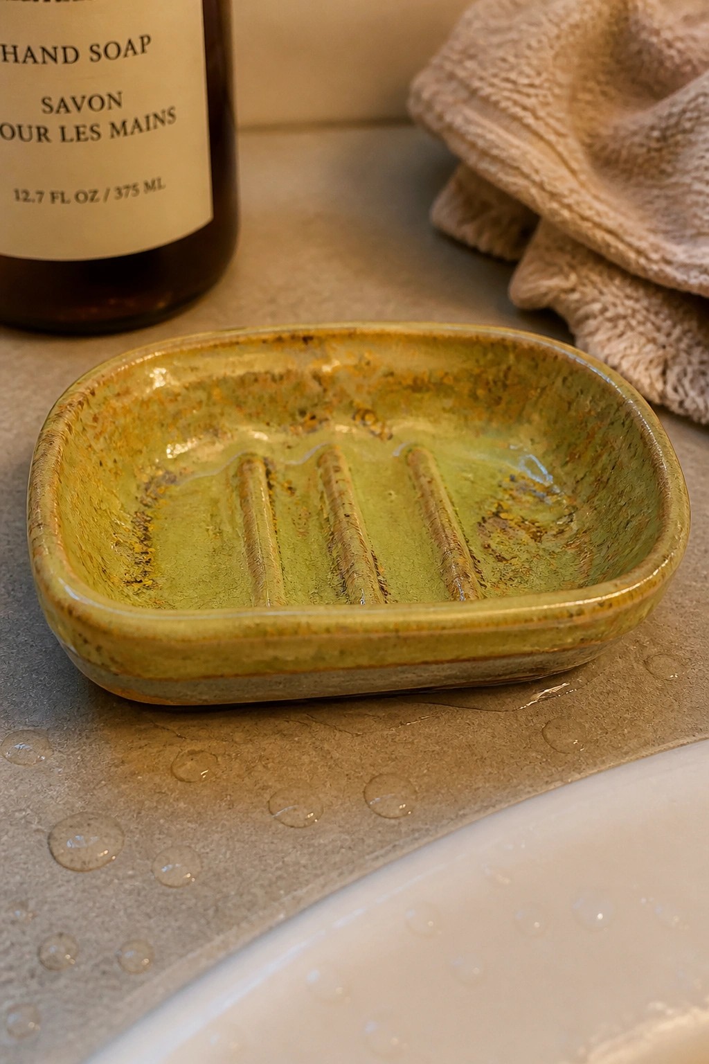 Green ceramic soap dish with ridges on wet bathroom countertop near soap bottle