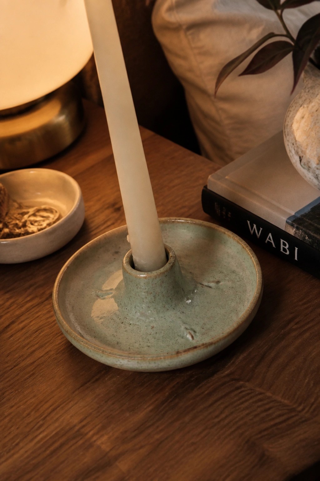 Green ceramic candle holder with white taper on wooden table with books