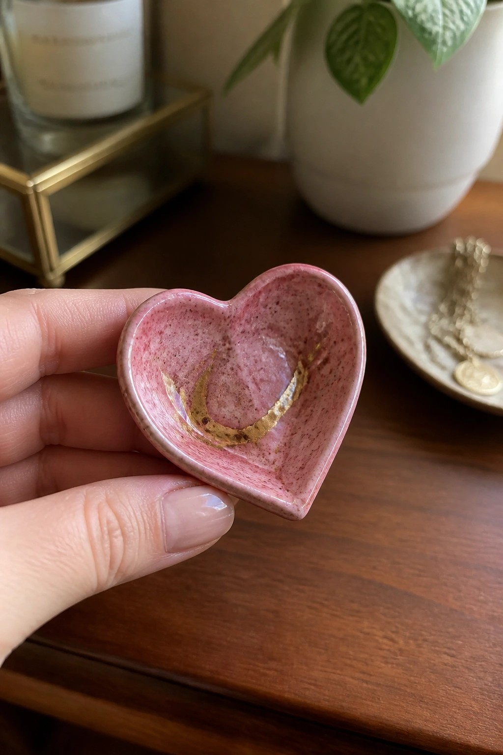 Hand holding pink speckled heart-shaped ceramic dish with gold accents