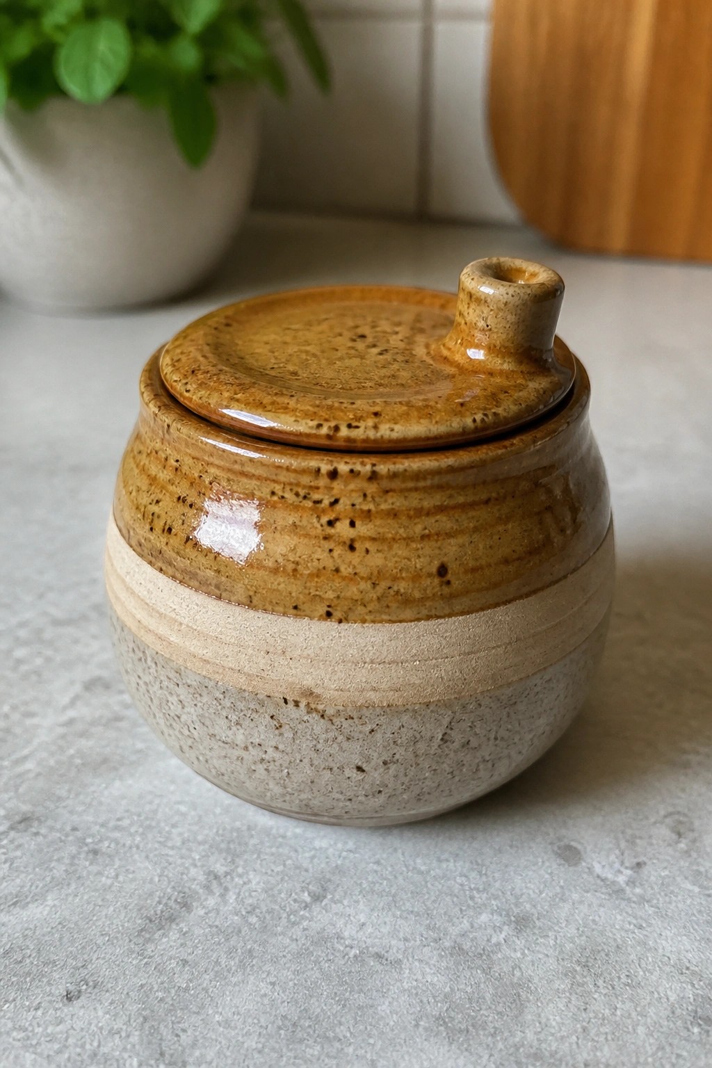 A small round ceramic jar with a lid, brown speckled glaze on the top half, and lighter matte glaze on the bottom half.