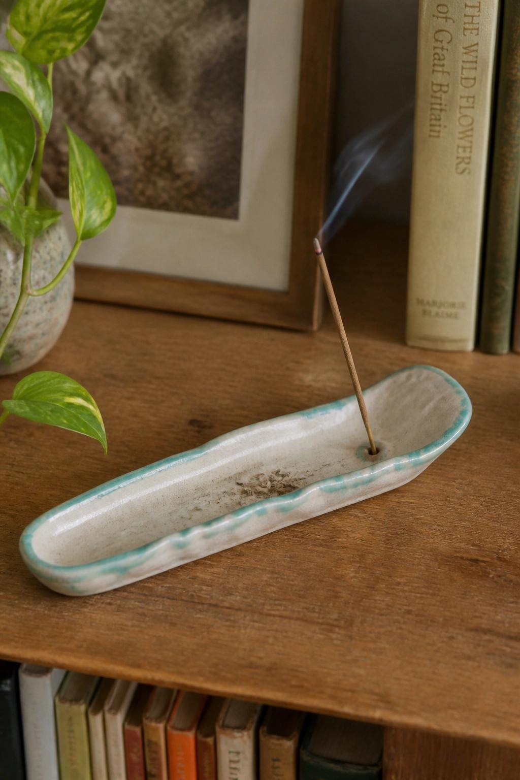 Burning incense stick in white ceramic holder with blue rim on wooden shelf