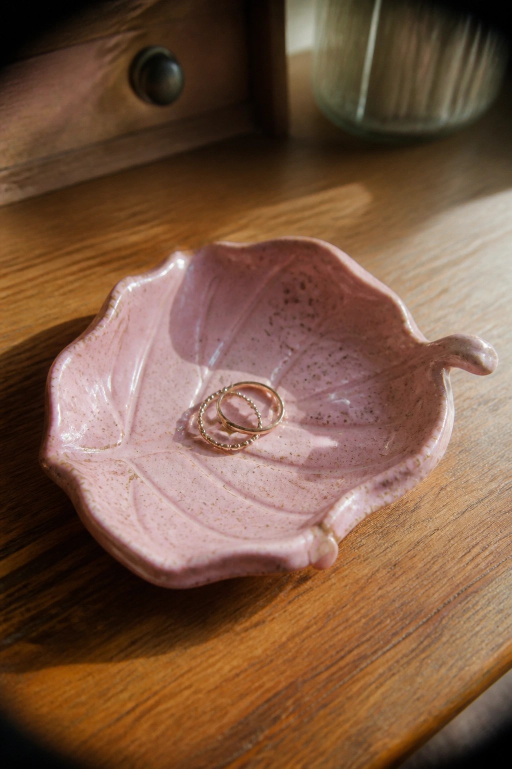 Pink ceramic leaf dish with two gold rings on wooden table
