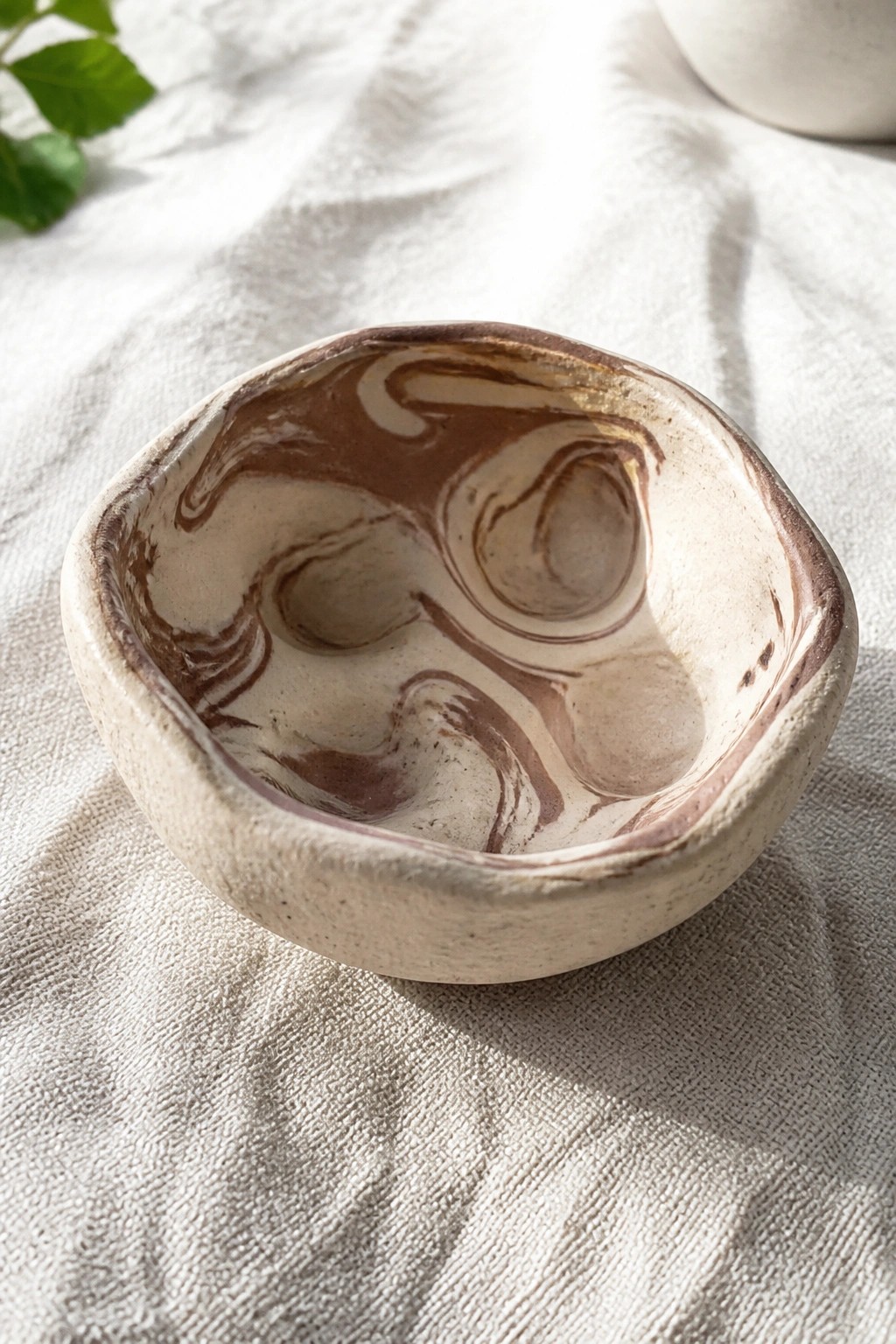 Rustic ceramic bowl with swirling brown and cream glaze on white linen fabric
