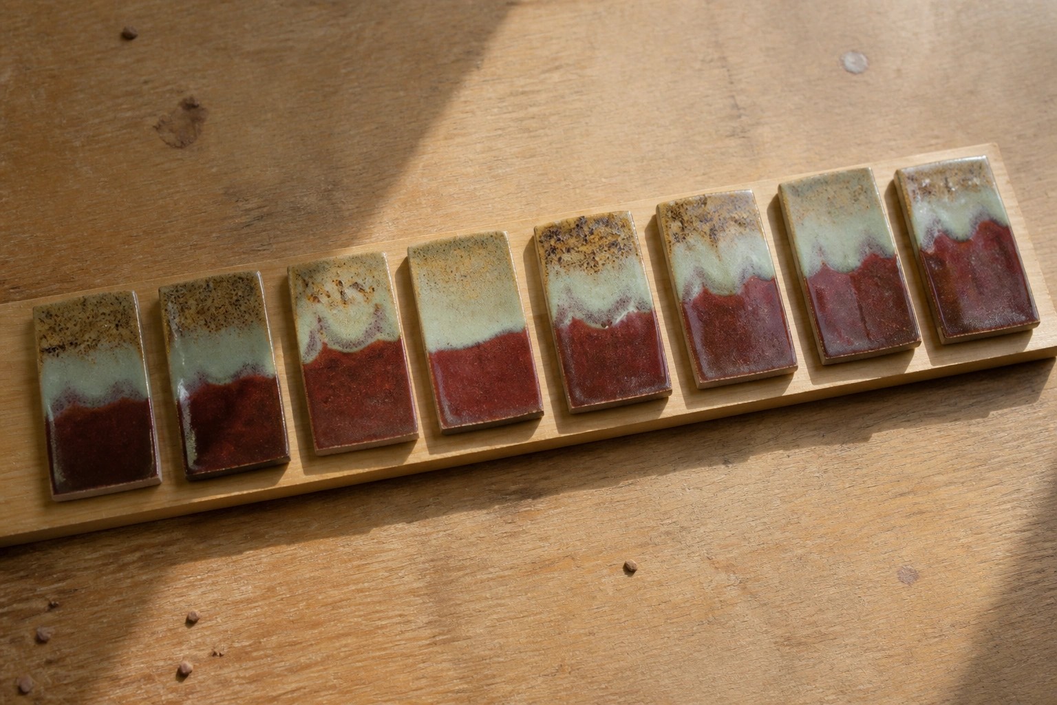 Seven numbered ceramic tiles on wood with red bases and speckled green glazes.