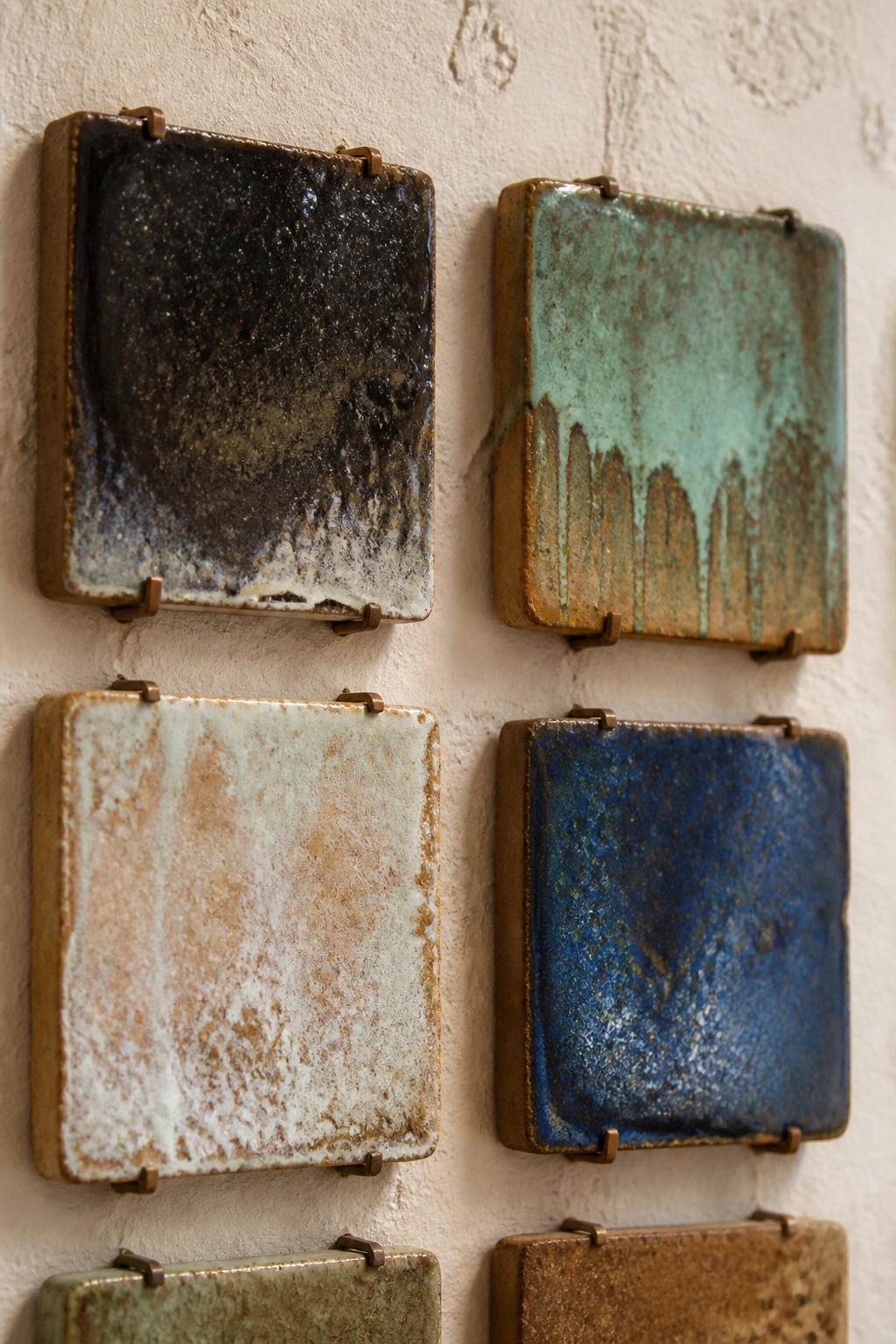 Assorted glazed ceramic tiles in blue, green, and brown on white wall