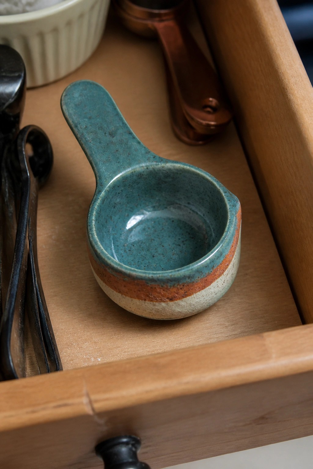 Teal ceramic bowl with handle in wooden kitchen drawer among utensils