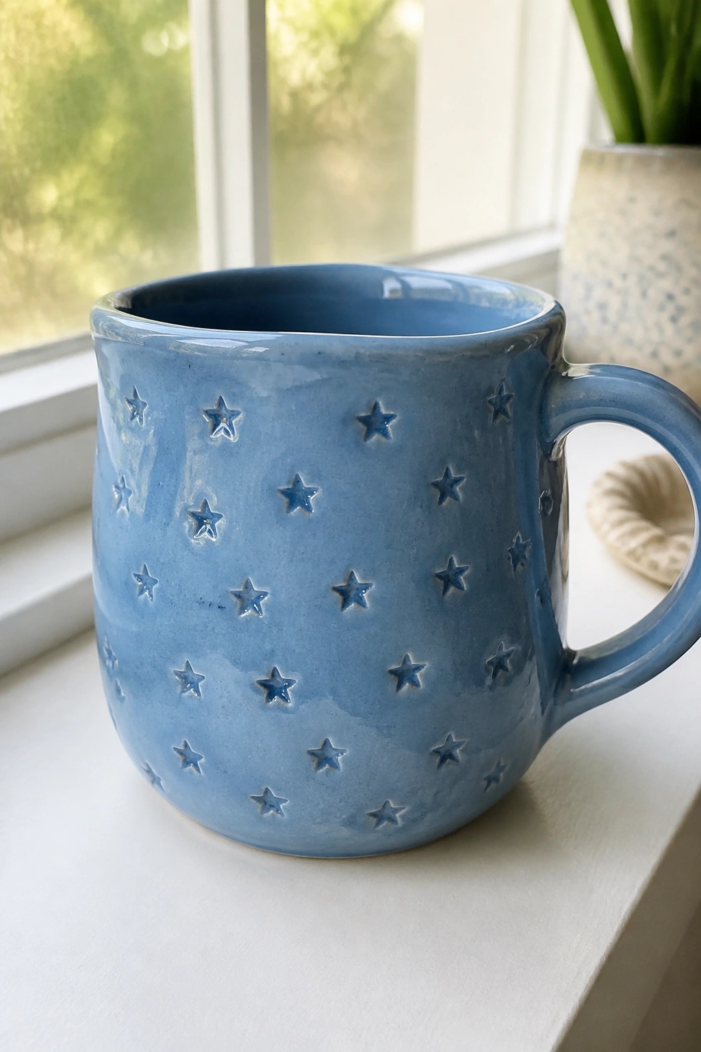 Blue ceramic mug with embossed stars on a white windowsill