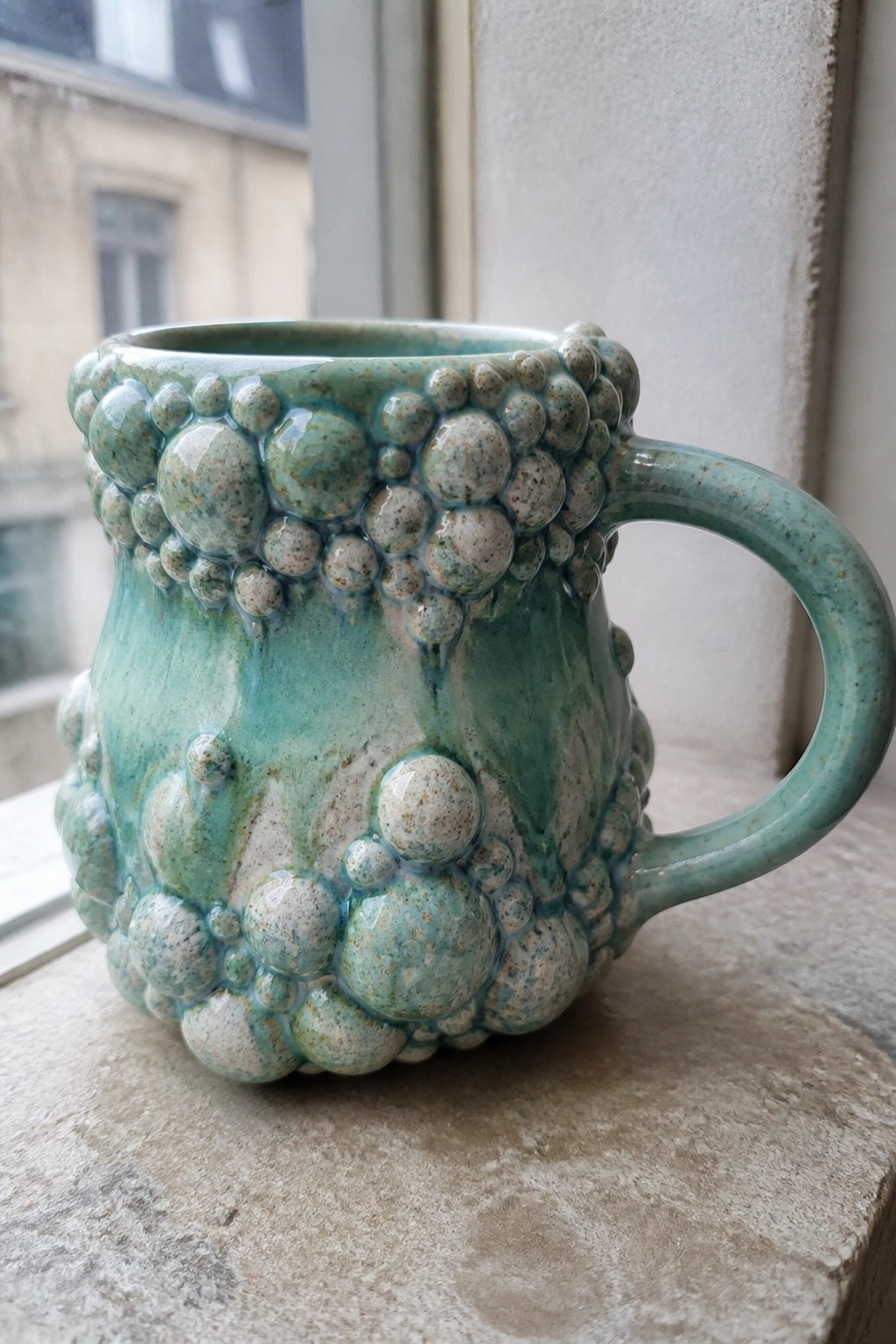 Turquoise ceramic mug with bubbly glaze texture on a windowsill.