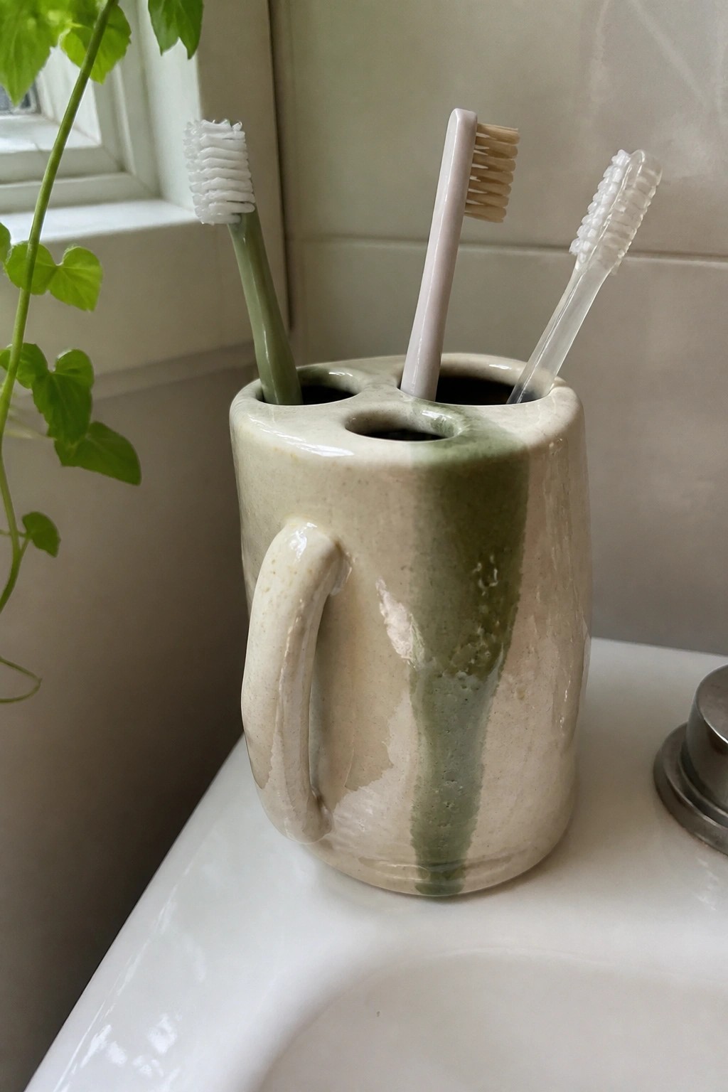 Three toothbrushes in a beige and green ceramic holder on a sink.
