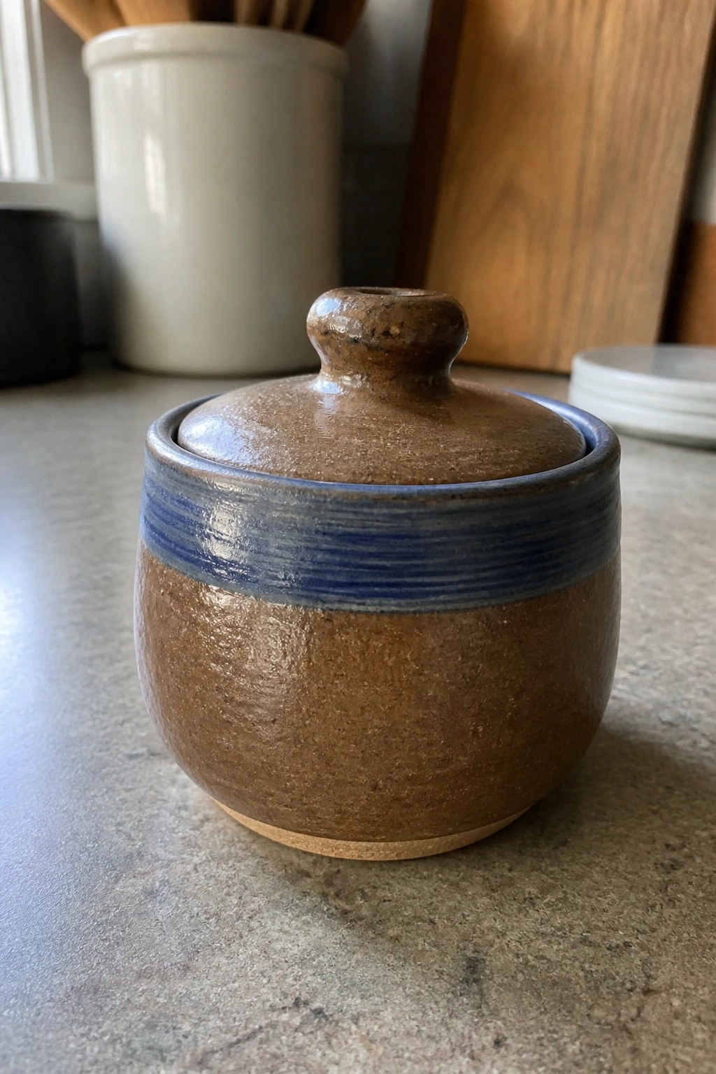 Brown ceramic lidded jar with blue band on kitchen countertop