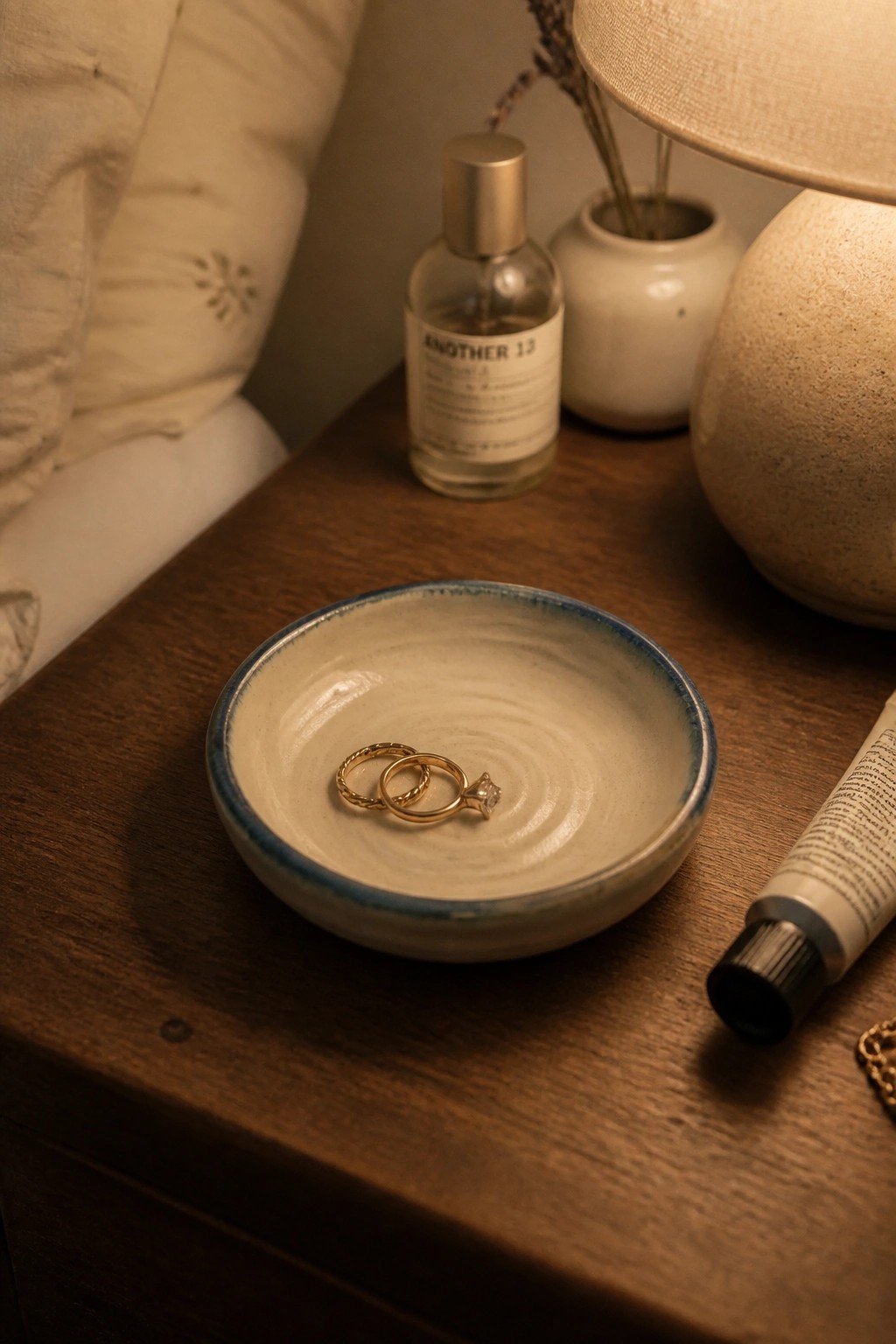 A small ceramic ring dish with a blue rim and cream interior holding two gold rings on a wooden surface.