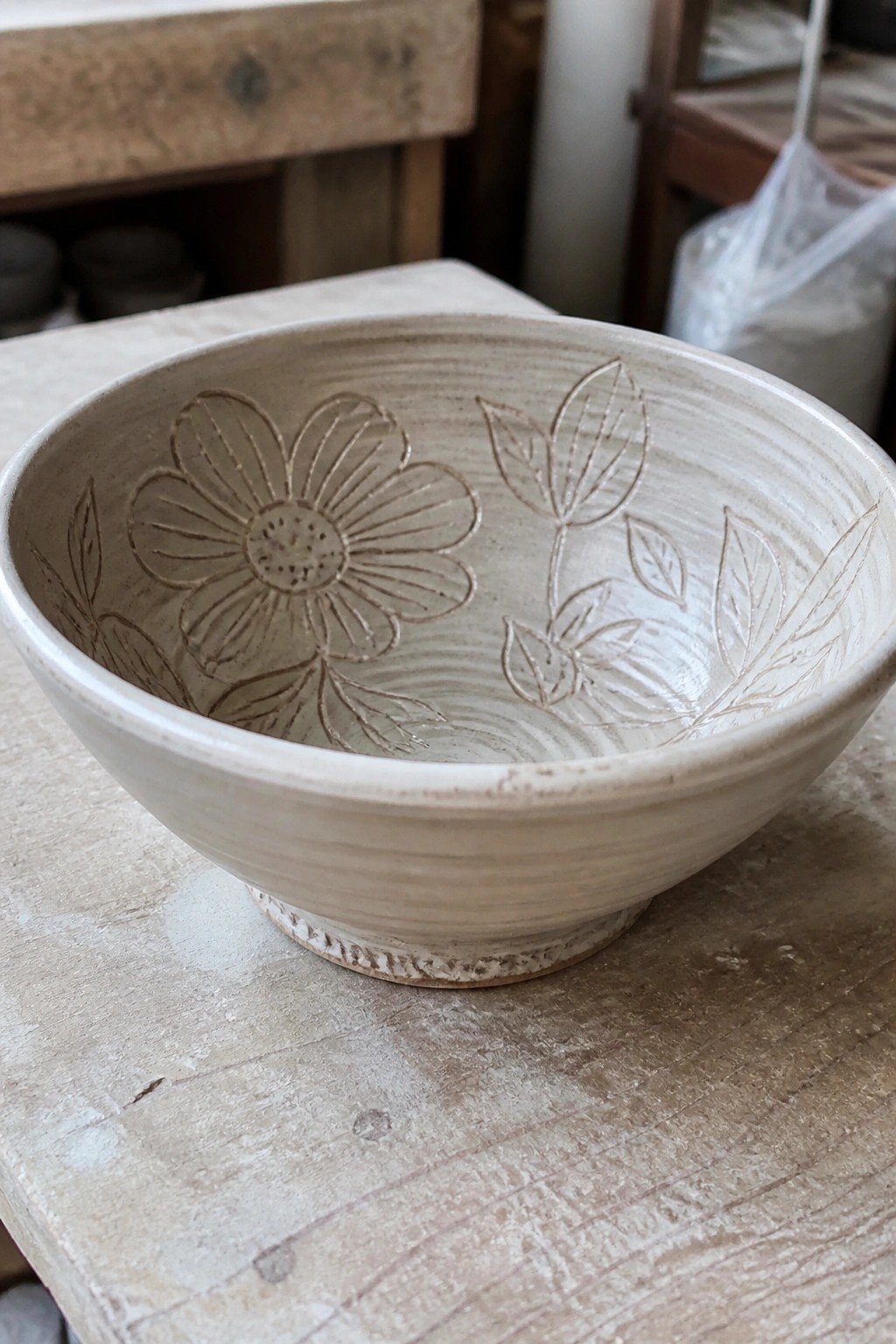 Light beige ceramic bowl with etched flower and leaf designs on wooden table
