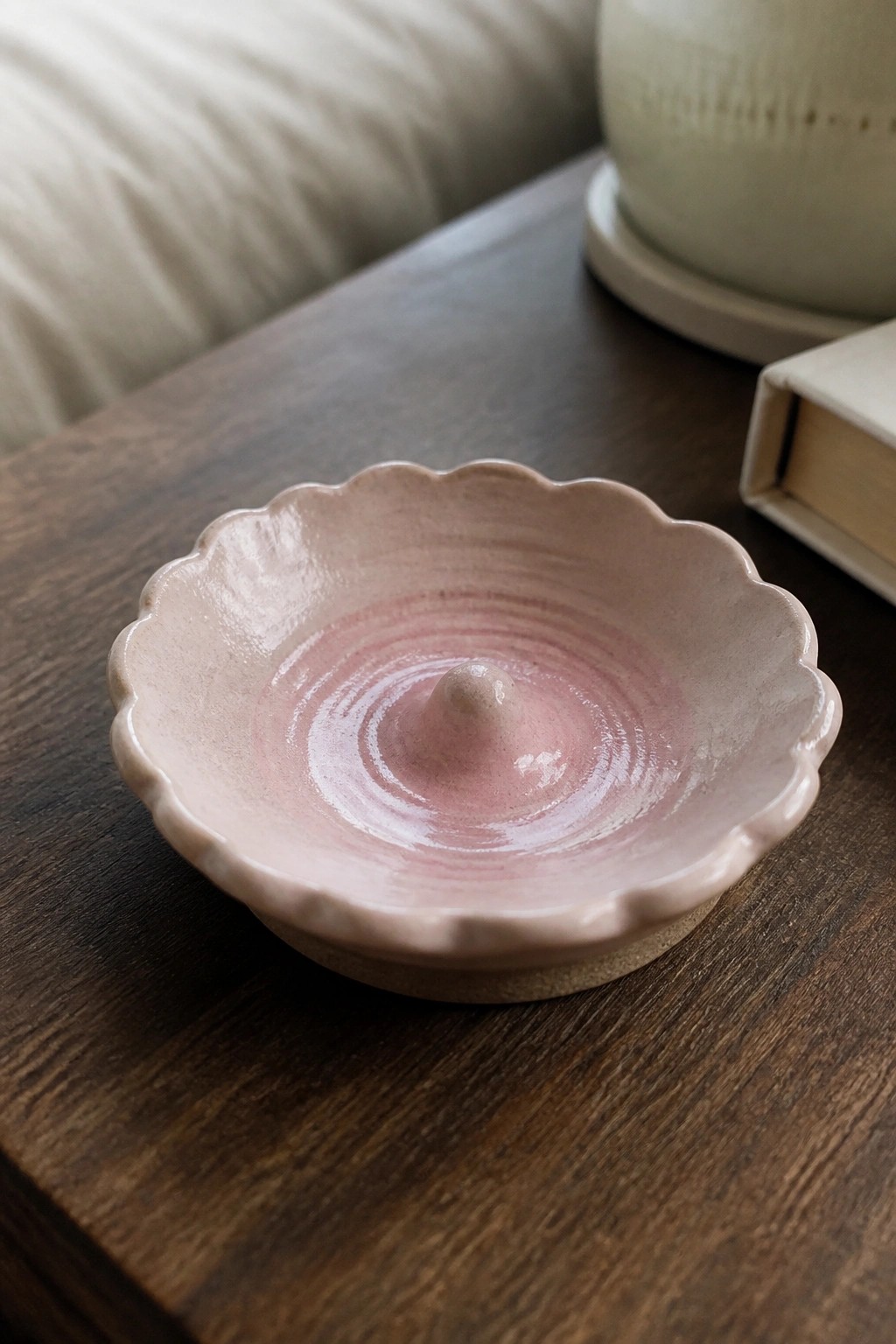 Pink scalloped ceramic dish with central knob on dark wooden table