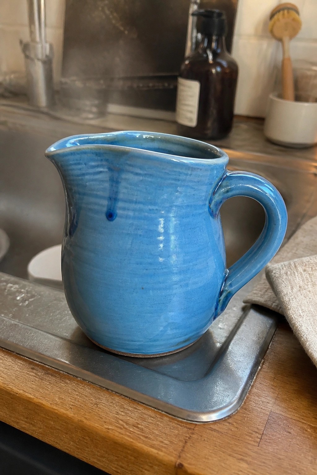 Blue ceramic pitcher with handle on metal tray over wooden kitchen counter