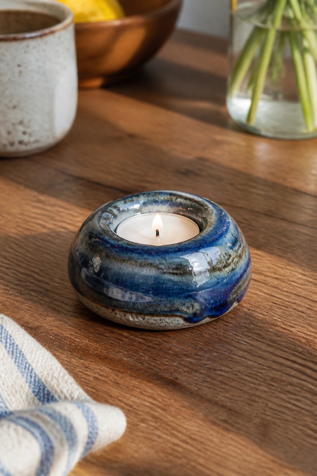 Blue ceramic tealight holder with lit flame on wooden table beside napkin