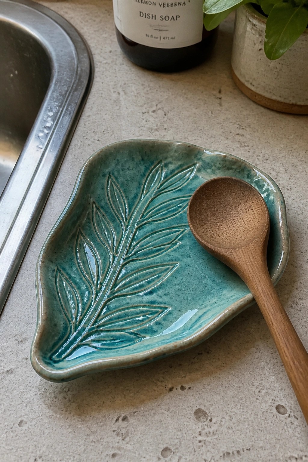 Teal ceramic leaf dish with wooden spoon on kitchen countertop near sink