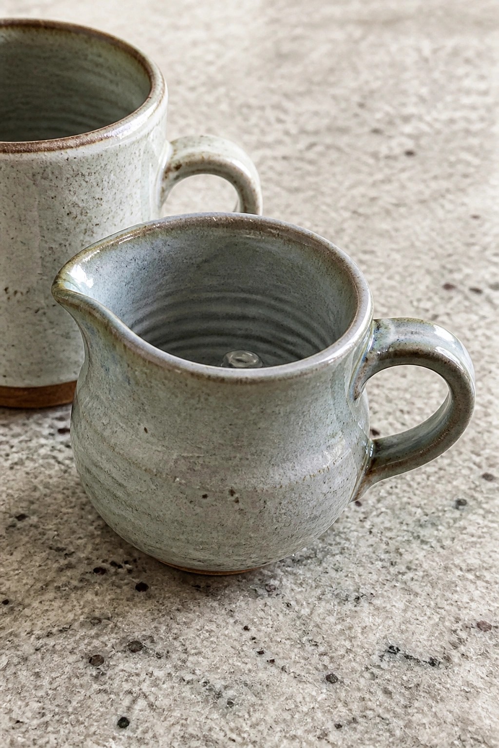Two rustic ceramic pitchers with handles on a speckled stone surface