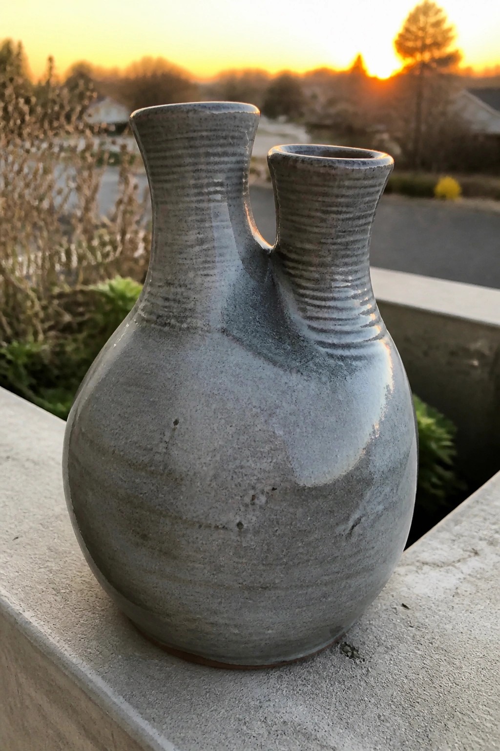 Gray ceramic vase with two necks on concrete ledge at sunset