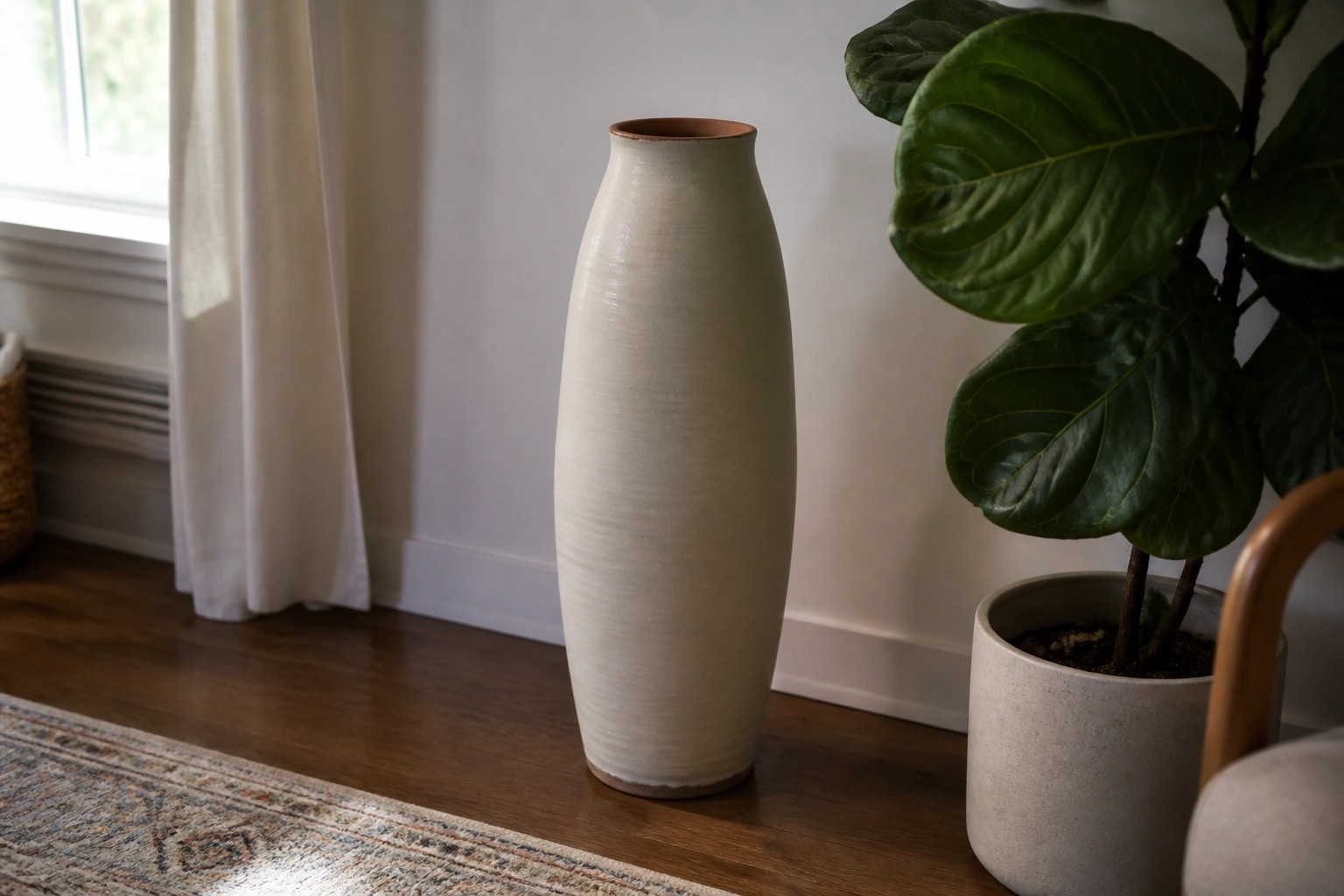 Tall off-white vase beside potted green plant on wooden floor