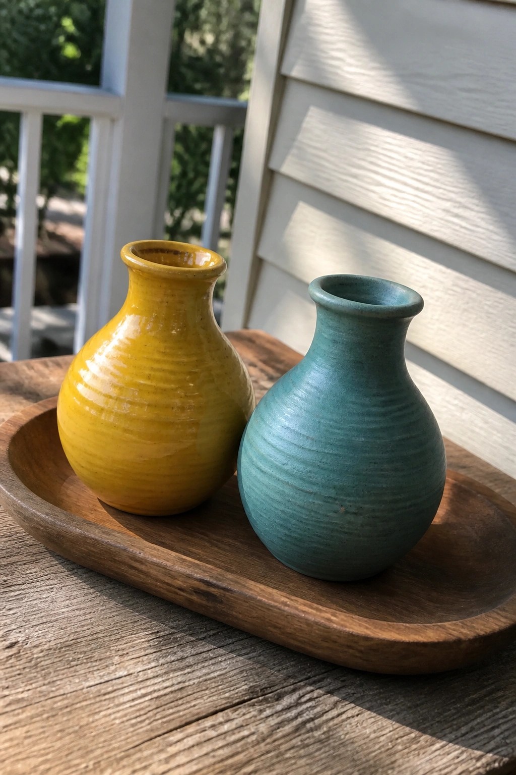 Yellow and teal ceramic vases on a round wooden tray outdoors