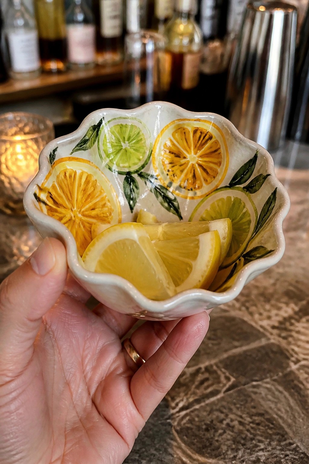 Hand holding scalloped ceramic bowl painted with lemons, limes, and fresh lemon wedges