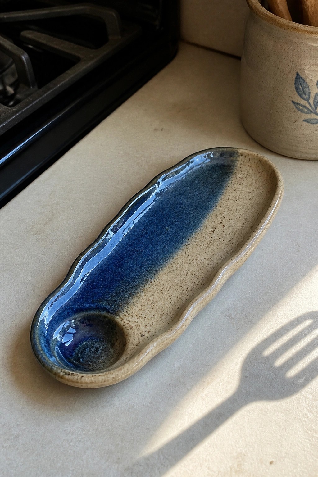 Blue and beige ceramic spoon rest on sunlit kitchen countertop near stove