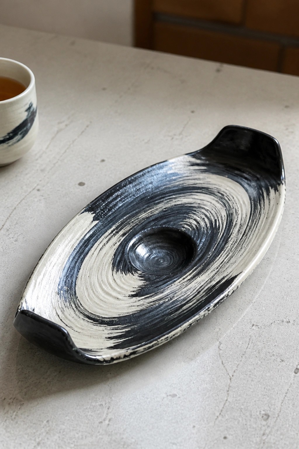 Elongated ceramic tray with swirling black and white glaze beside a small cup