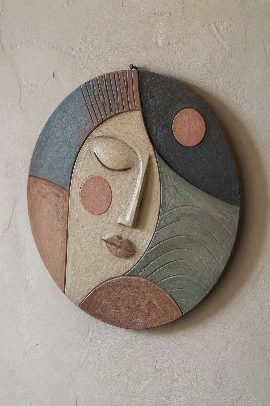 Circular abstract relief of a stylized woman's face in muted geometric colors.