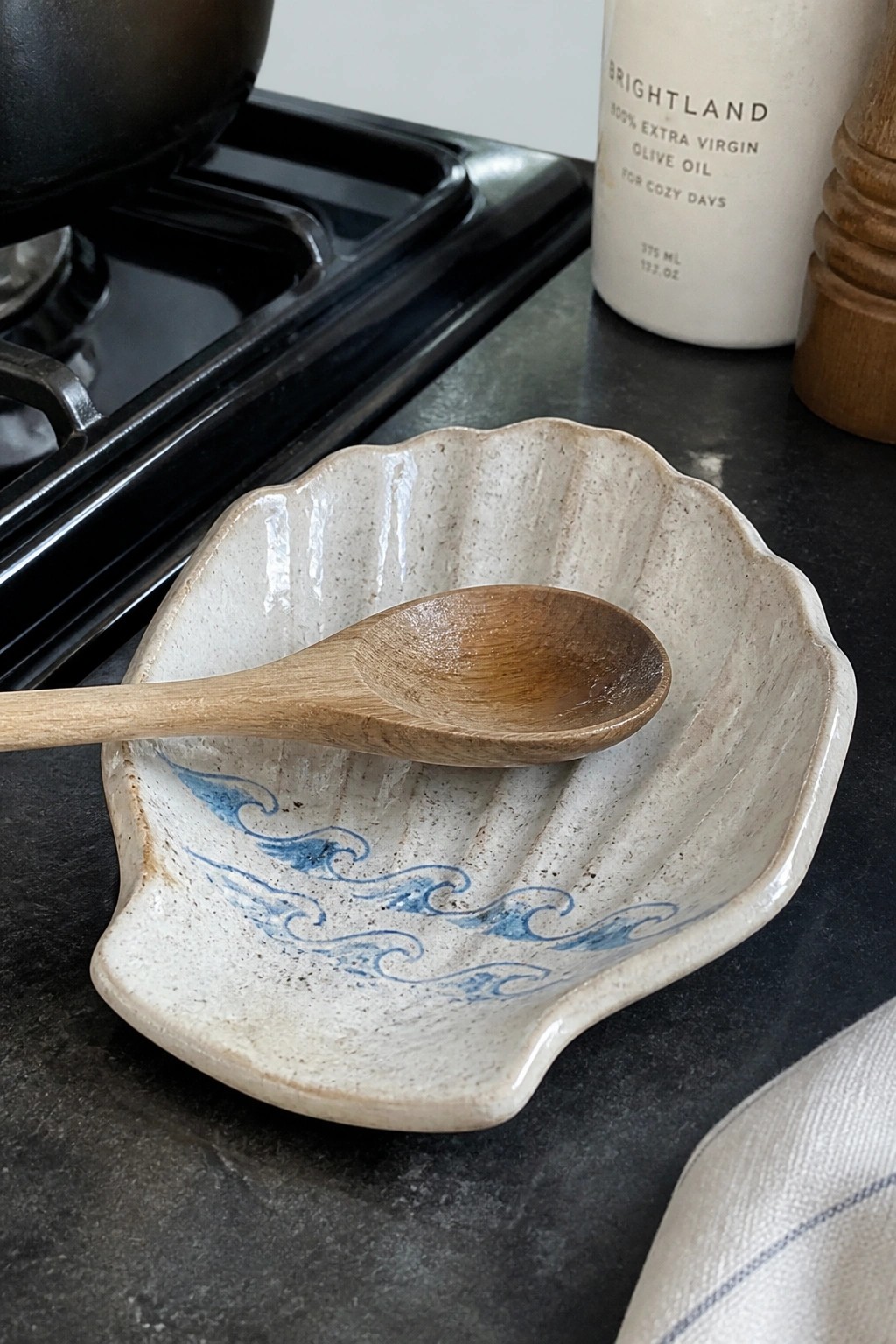 Wooden spoon resting in shell-shaped ceramic dish with blue waves on kitchen counter
