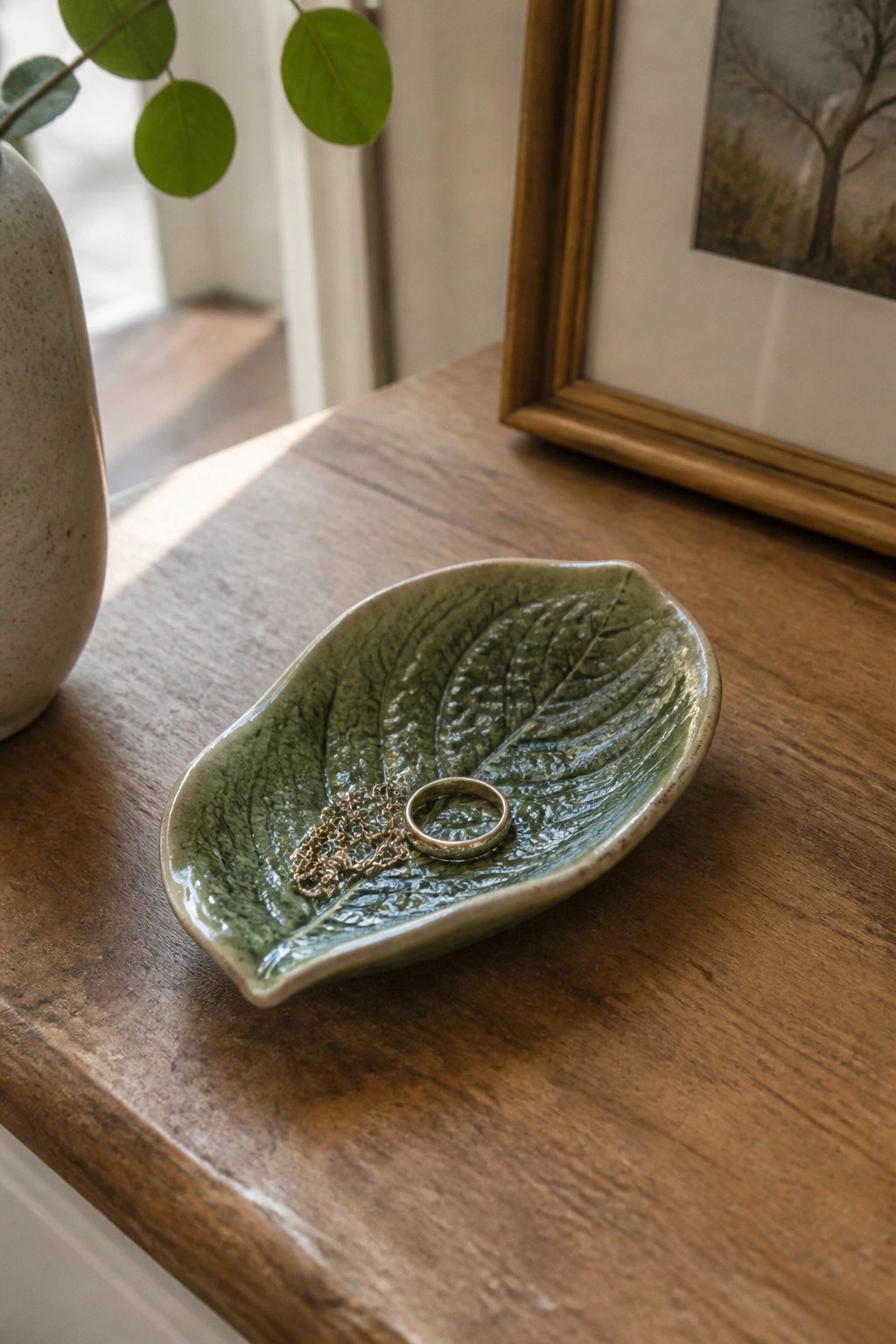 Green leaf-shaped ceramic dish with gold ring and chain on wooden table