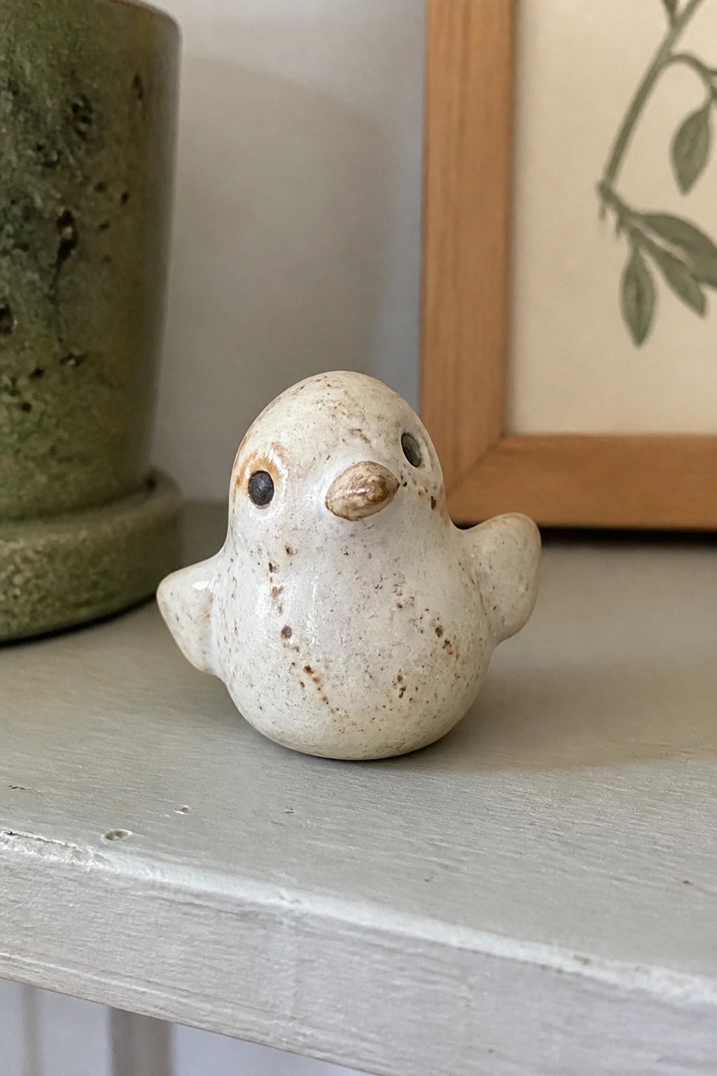 Small speckled white ceramic bird figurine on light gray wooden shelf