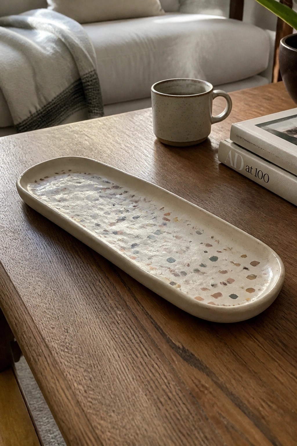 Oval speckled terrazzo tray beside mug and books on wooden coffee table