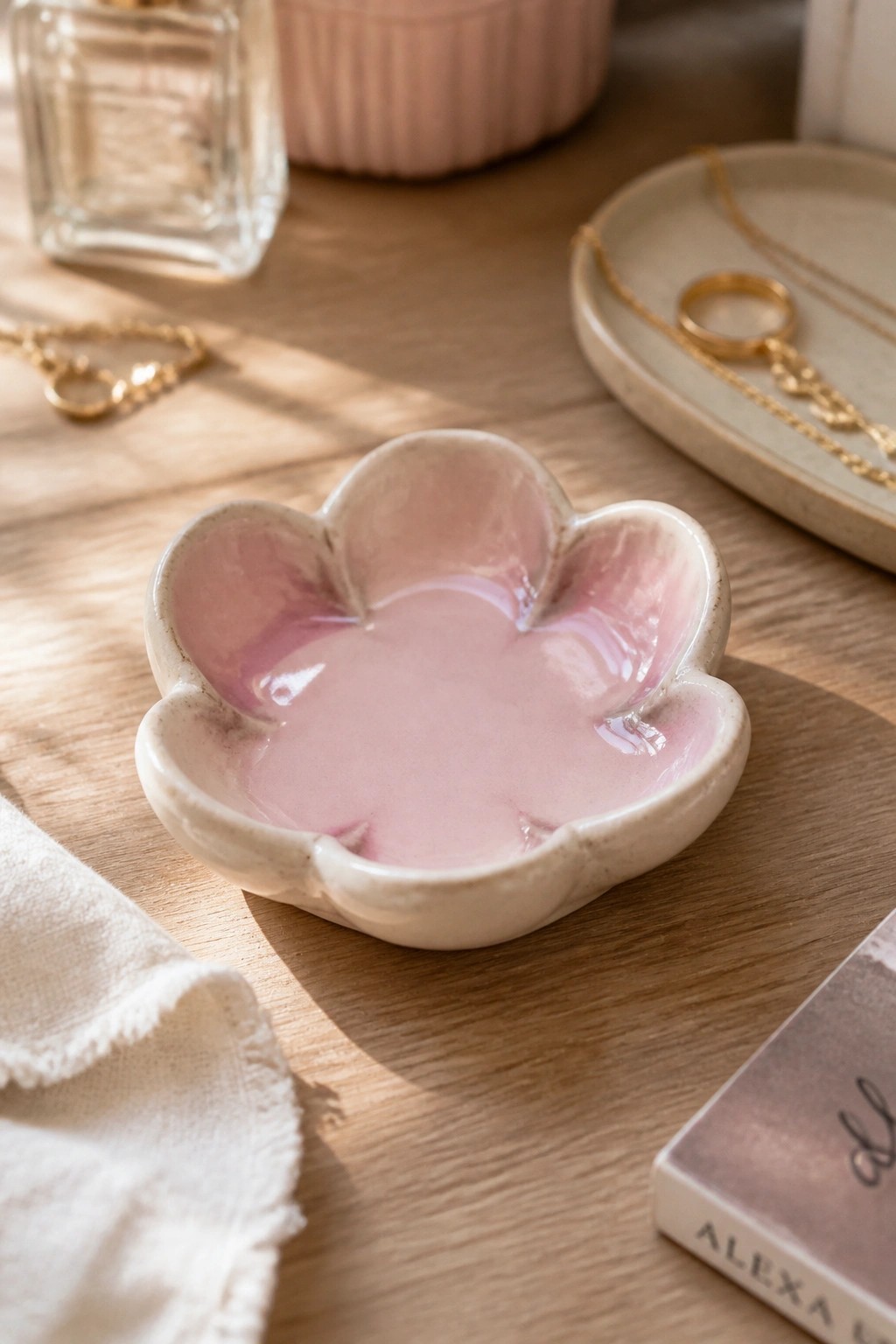 Pink marbled ceramic paw-shaped dish on wooden table with gold jewelry nearby.