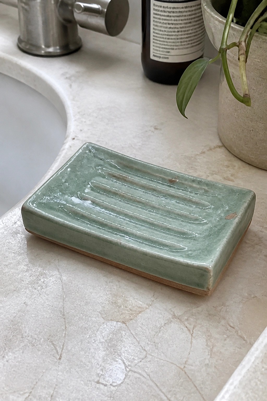 Green ridged ceramic soap dish on white marble bathroom countertop