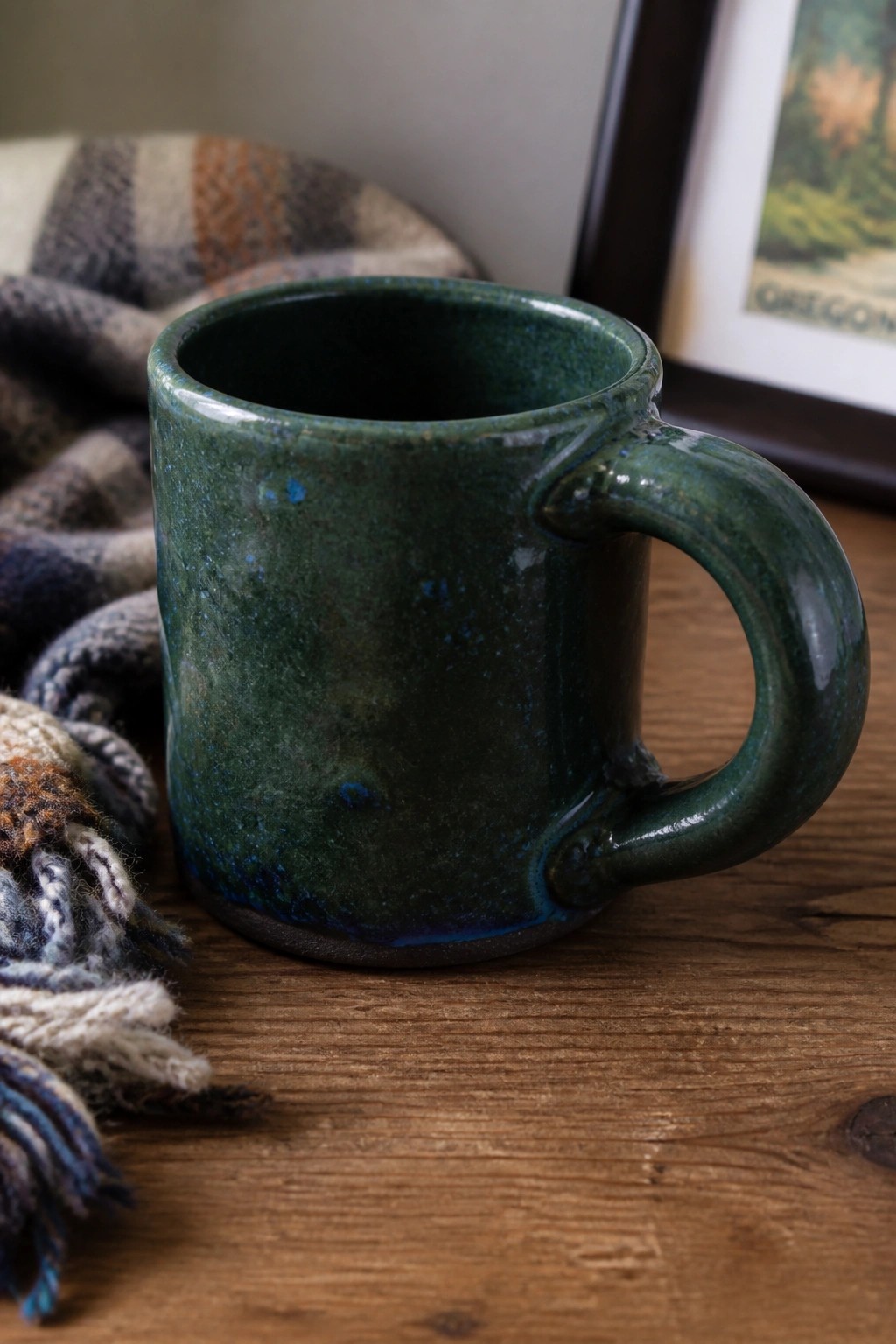 Green glazed ceramic mug on wooden table beside plaid blanket and Oregon frame