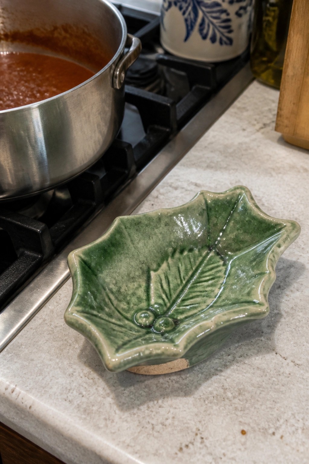 Green leaf-shaped ceramic bowl beside pot of red sauce on kitchen stove