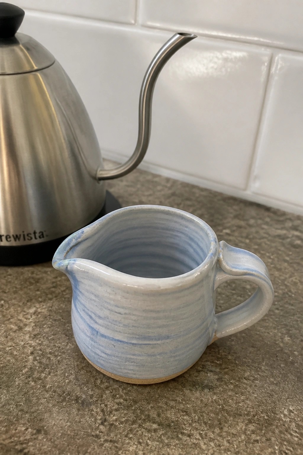 Blue striped ceramic pitcher beside stainless steel gooseneck kettle on counter