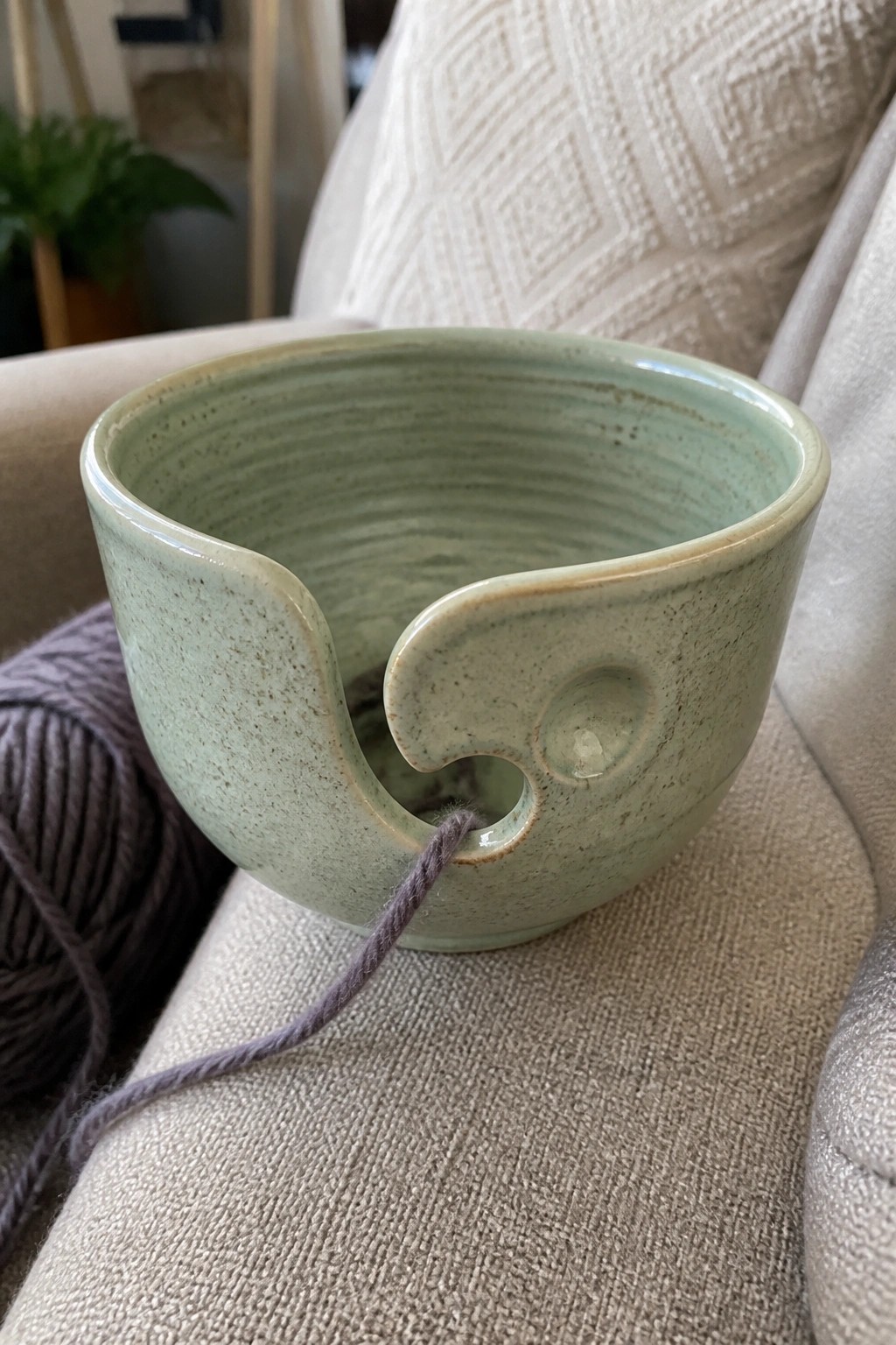 Light green speckled ceramic yarn bowl with purple strand on beige couch