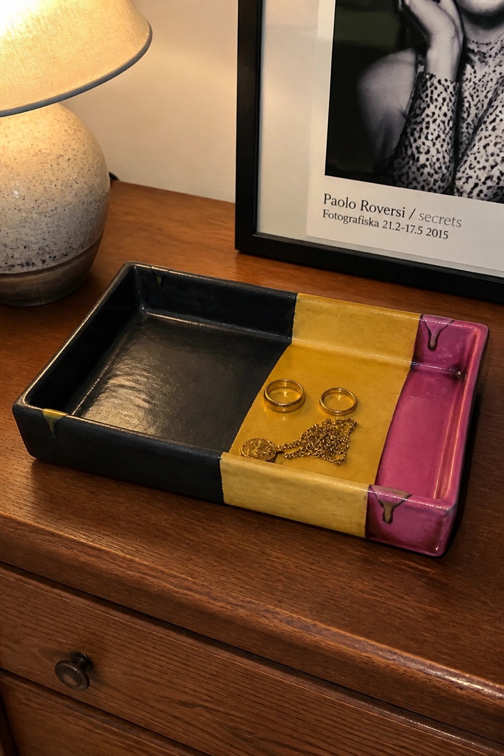 Tri-color ceramic tray holding two gold rings and chain necklace on wood