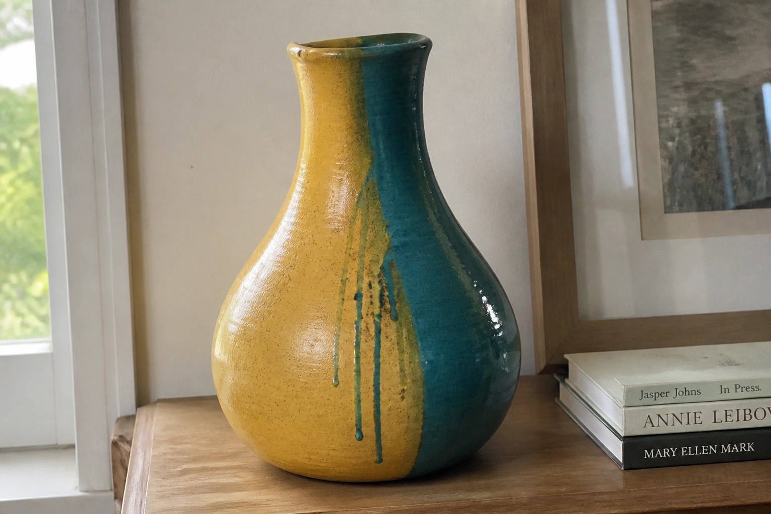 Yellow and teal ceramic vase with dripping glaze on wooden shelf