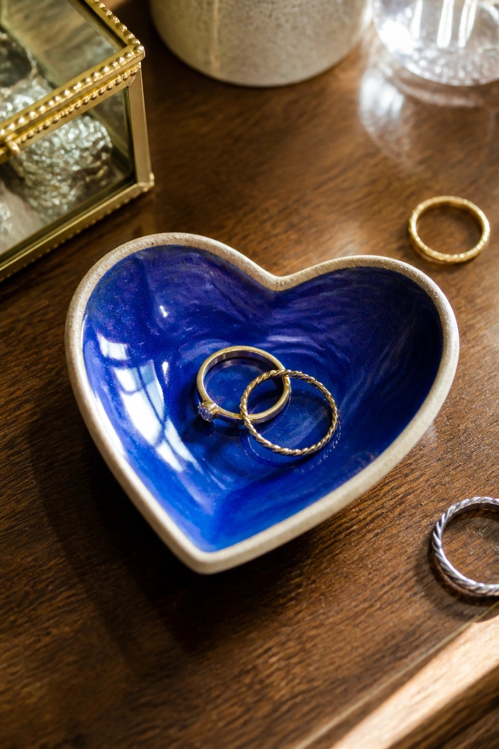 Blue heart-shaped ceramic bowl holding diamond and twisted gold rings on wood