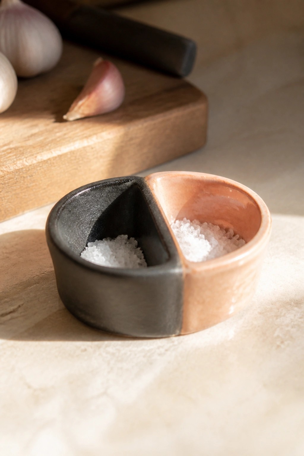 Two-toned black and terracotta ceramic bowl with salt, garlic on wooden board.