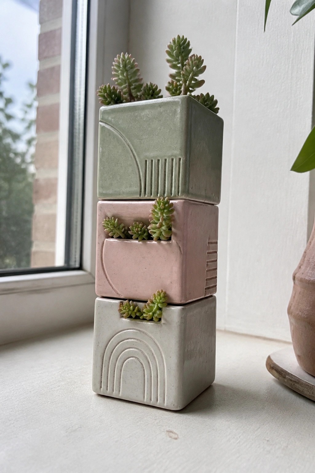 Stacked sage green, pink, and white ceramic planters with succulents on a windowsill.